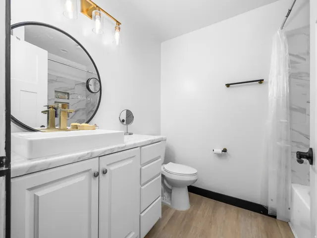 White shaker-style vanity with a vessel sink, a round black-framed mirror, and a brass-finish light fixture