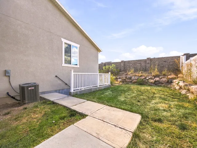 Stucco exterior with a white-framed window, concrete pathway, and a grassy area