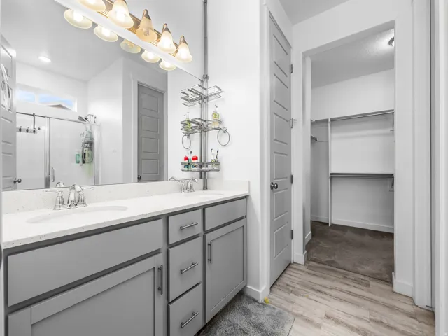 Dual vanity with light gray cabinetry and white countertops, chrome faucets, and a full-width mirror