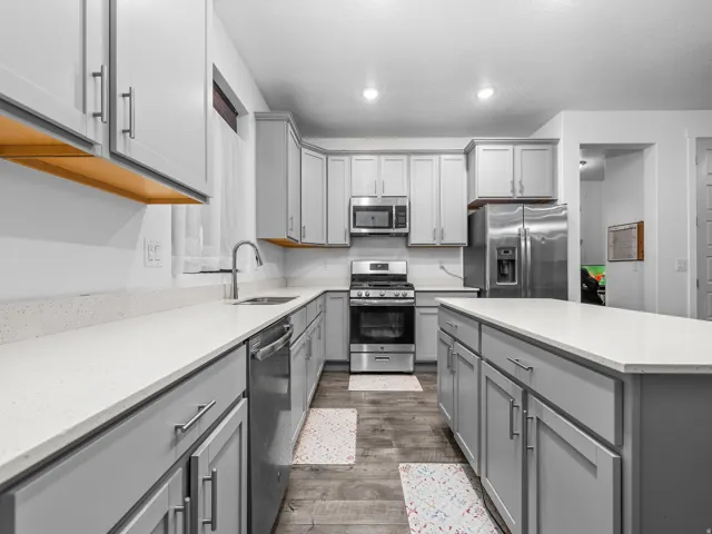 Well-appointed kitchen featuring light gray cabinetry, stainless steel appliances, white countertops, a central island, and wood-finish flooring