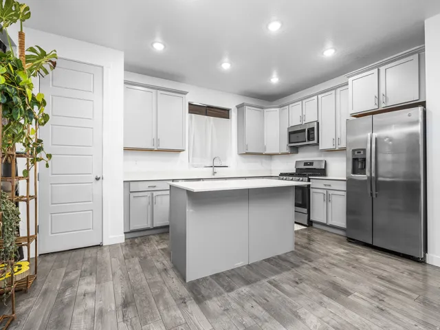 White shaker-style cabinetry with integrated hardware, stainless steel appliances, a center island with a solid surface countertop, wood-finish flooring, and recessed lighting