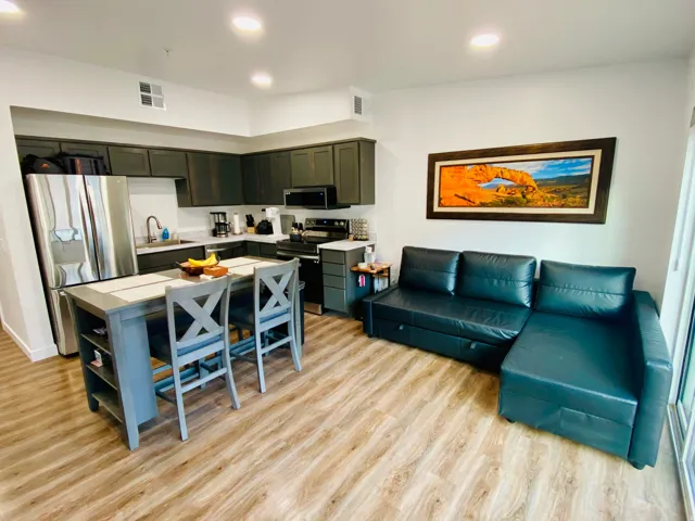 Open-concept living area featuring wood-finish flooring, dark kitchen cabinetry, stainless steel appliances, and recessed lighting