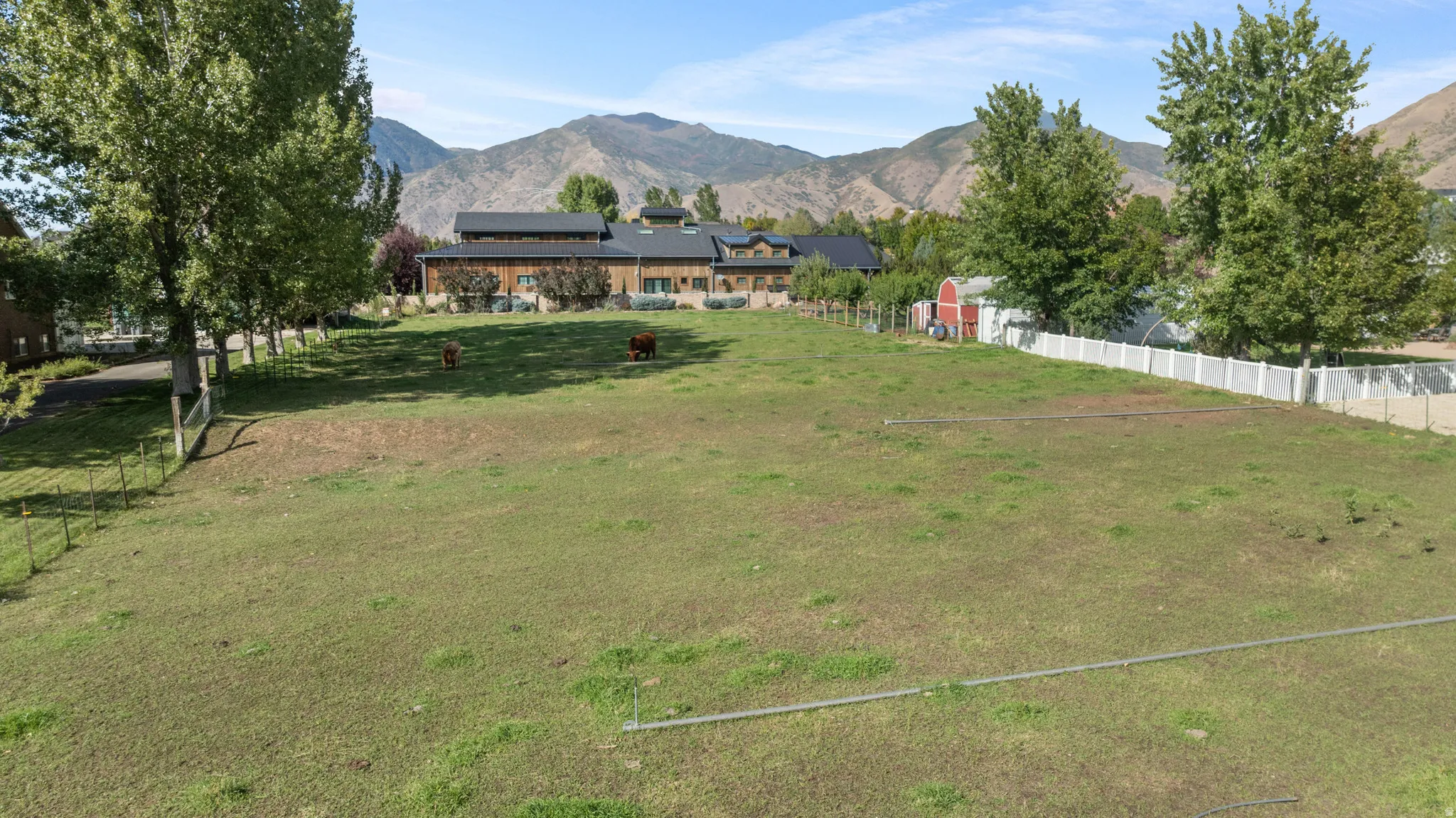 Expansive green space with distant mountain backdrop, featuring a barn structure and mature trees