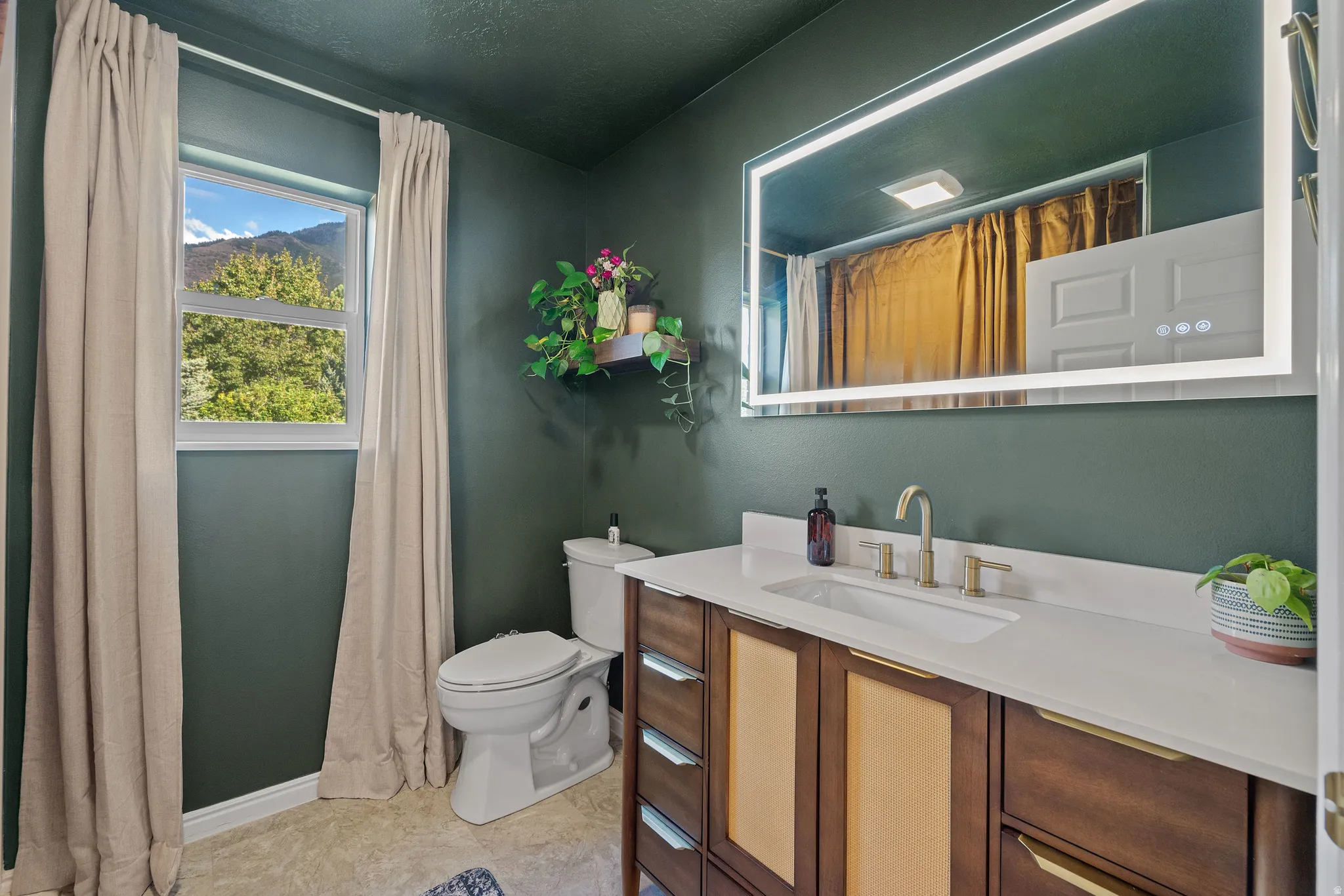 Bathroom featuring a wood-finish vanity with an integrated sink, a large back-lit mirror, and a window