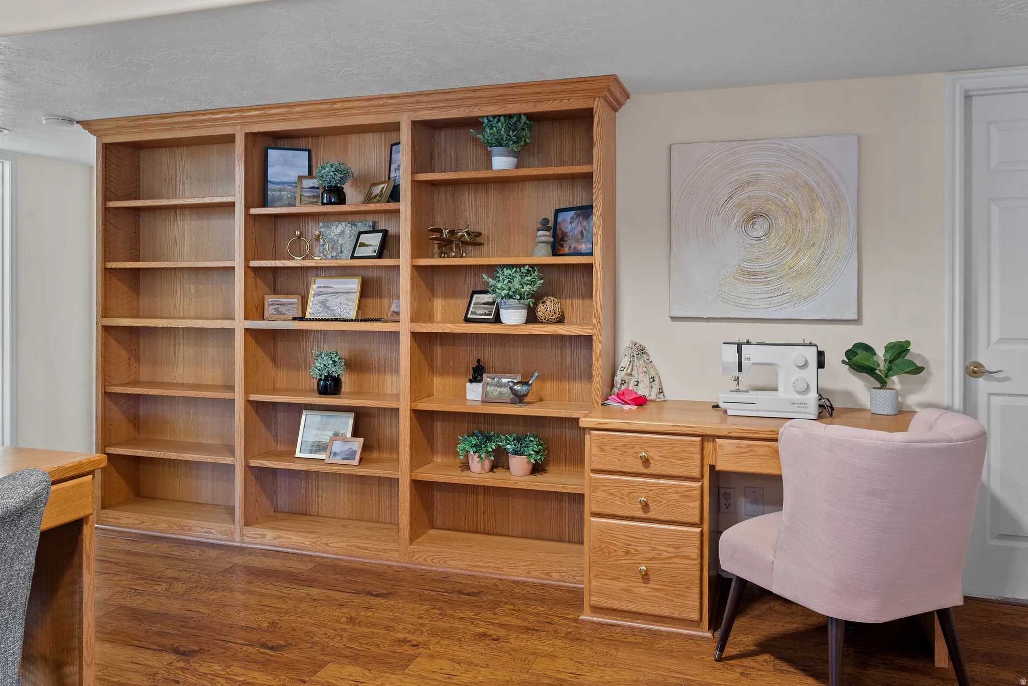 Built-in wood-finish shelving with crown molding, wood-finish flooring, and a dedicated desk area with storage drawers