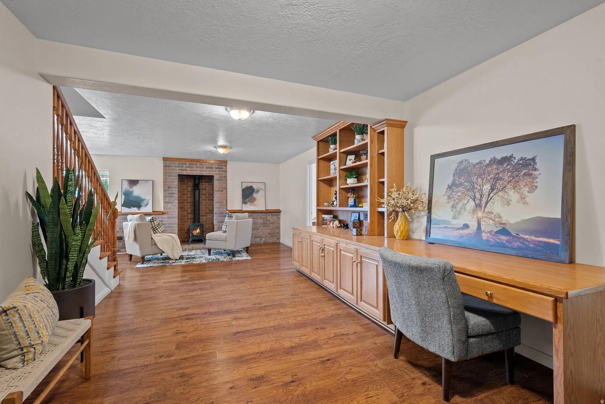 Wood-finish flooring throughout, built-in shelving, wooden staircase with balusters, exposed brick fireplace, and integrated desk