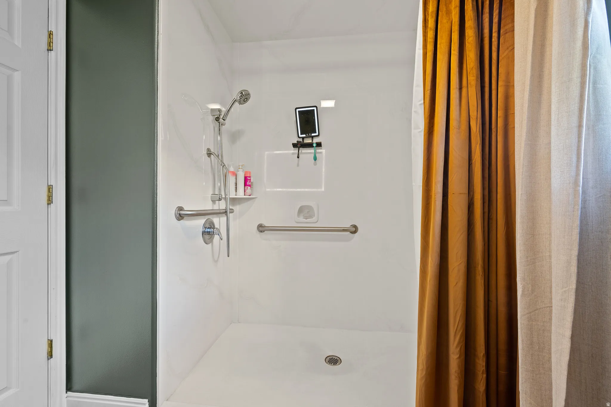 White shower stall featuring a built-in shelf, grab bars, and a handheld showerhead