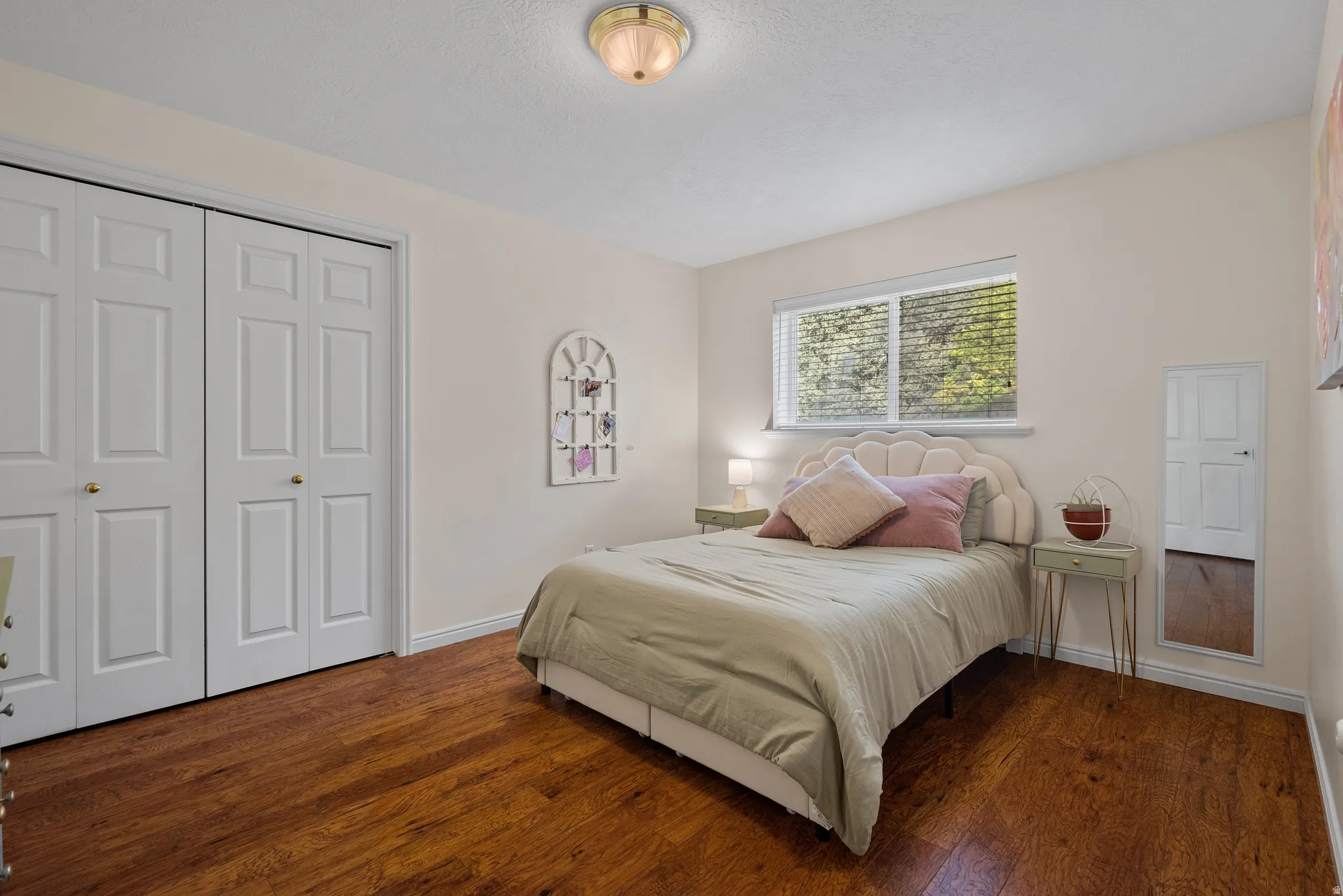 Wood-finish flooring, white bi-fold closet doors, wall-mounted light fixture, white interior walls, and a window with blinds