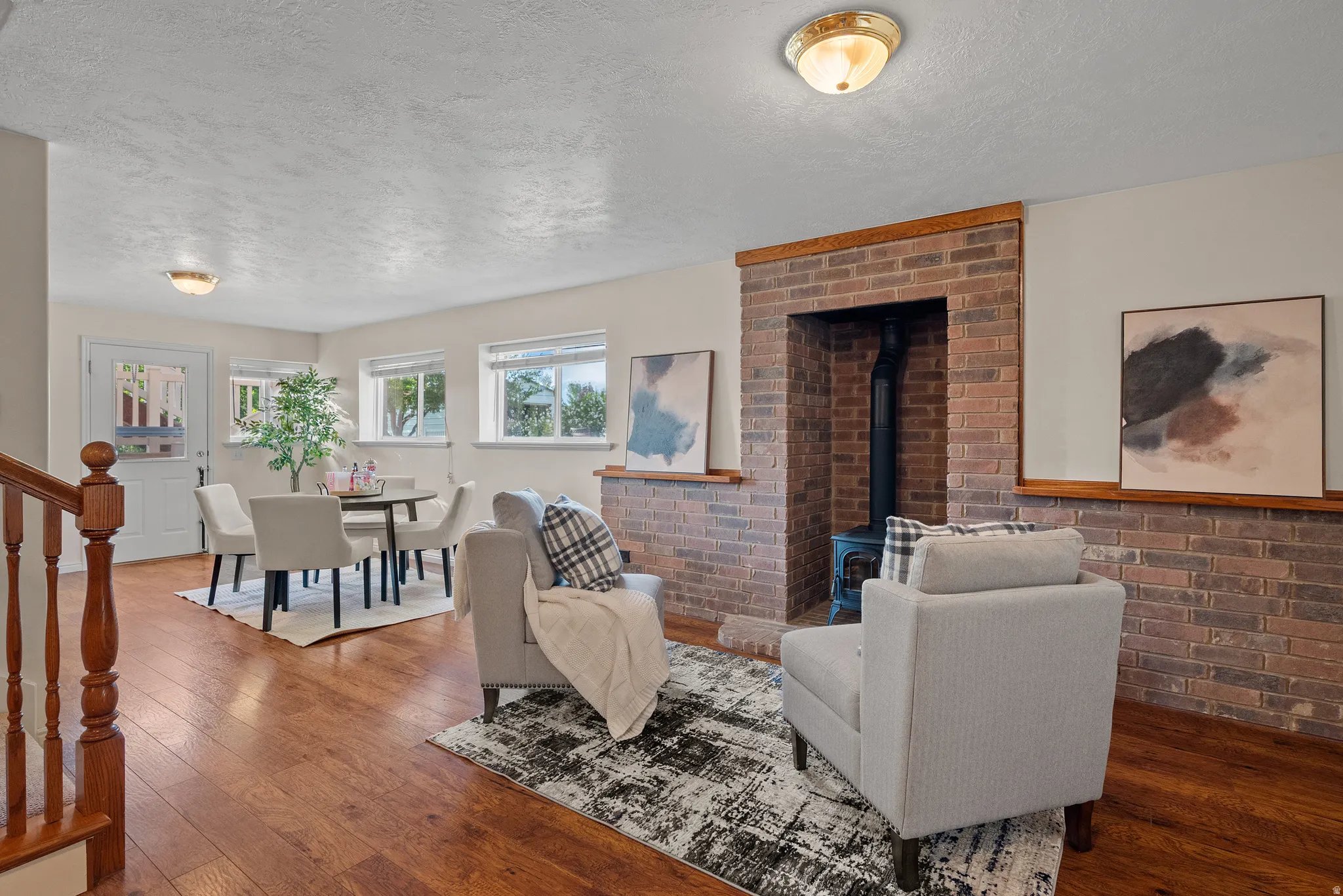 Wood-finish flooring throughout, brick accent wall with fireplace, multiple windows, and a glass-paneled door