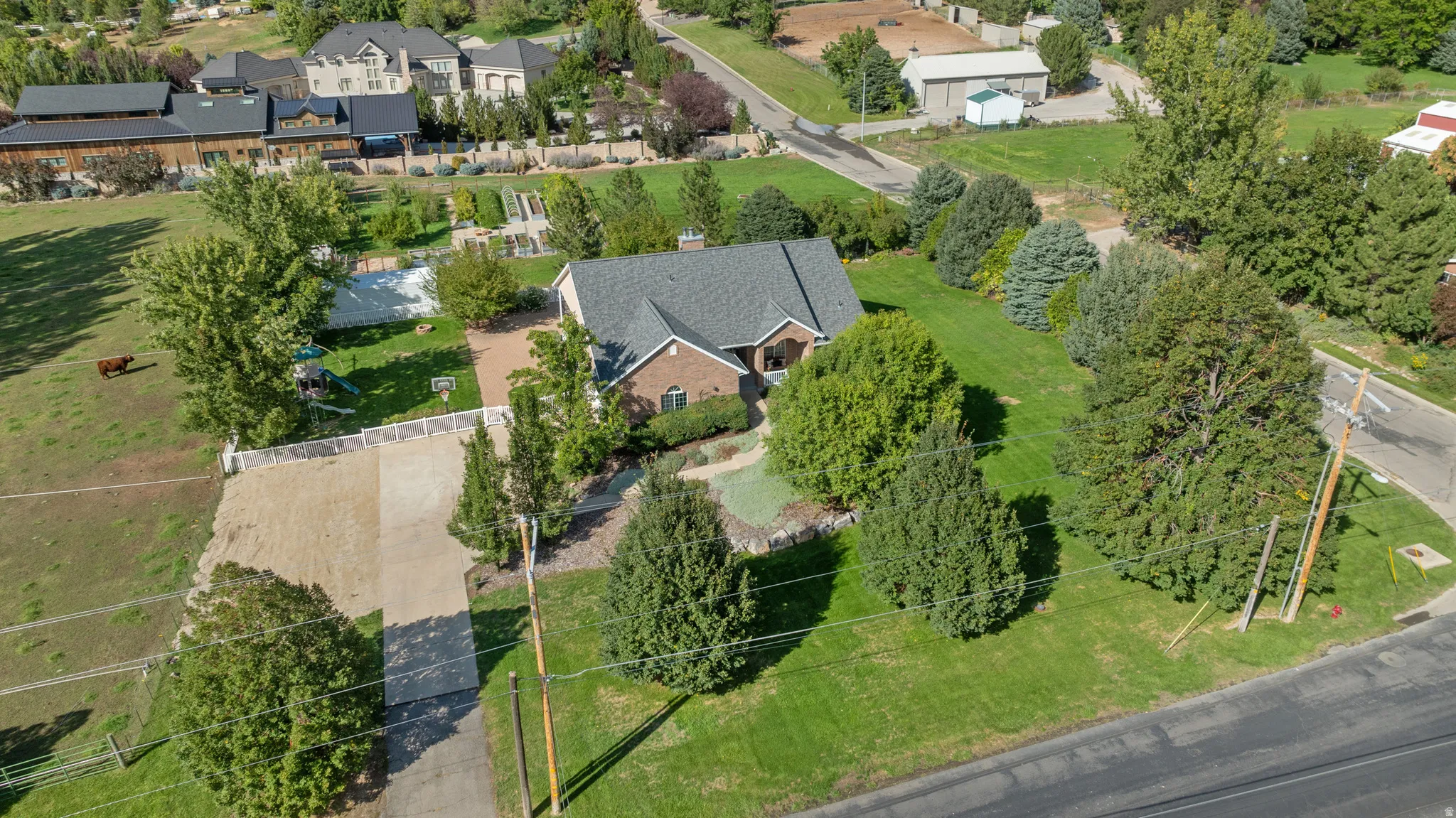 Brick exterior residence with a dark shingle roof, extensive green lawn, mature trees, and a gravel driveway
