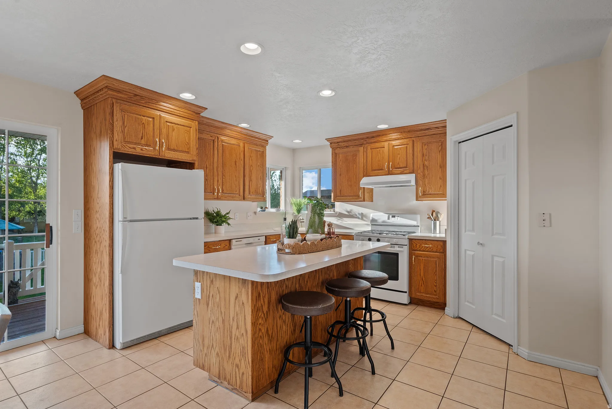 Kitchen featuring wood cabinetry, a center island with countertop seating, a white appliance package, and tile flooring