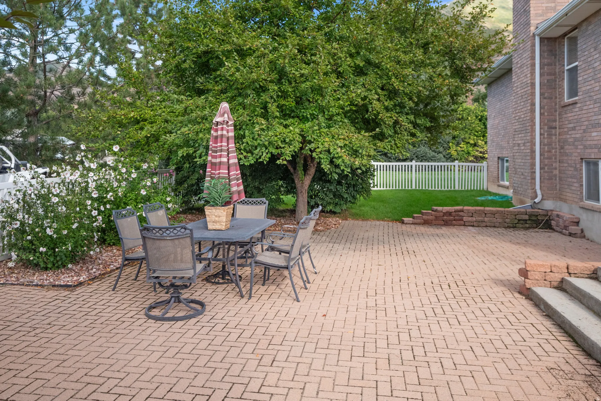 Expansive brick paver patio featuring a herringbone pattern, bordered by mature trees and lush landscaping