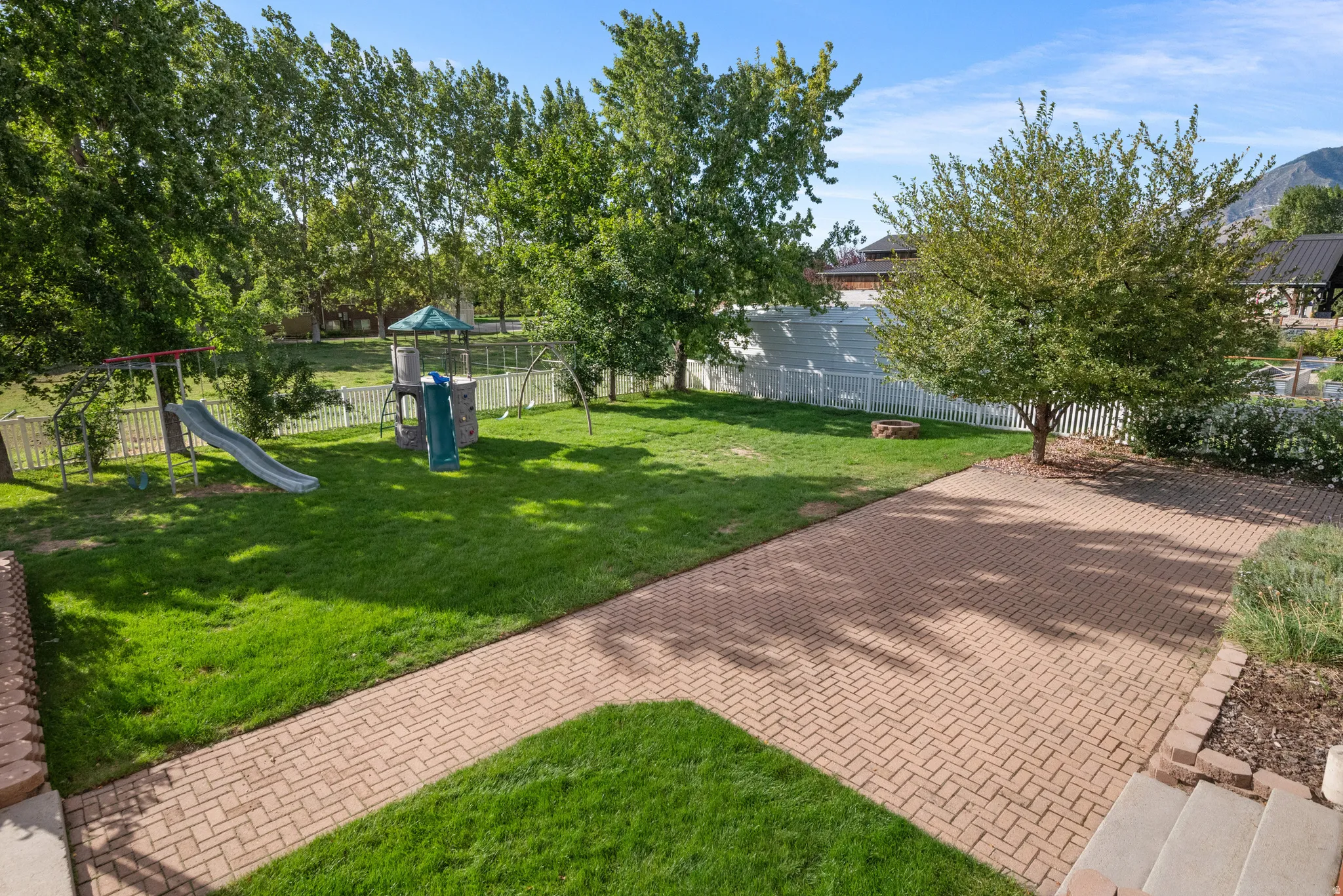 Expansive backyard featuring a paver patio, manicured lawn, and mature trees