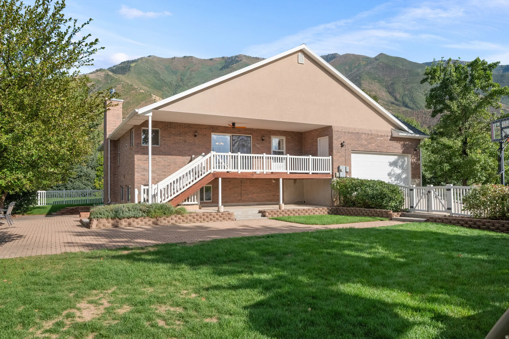 Brick exterior with covered deck, lower patio, attached two-car garage, and expansive lawn