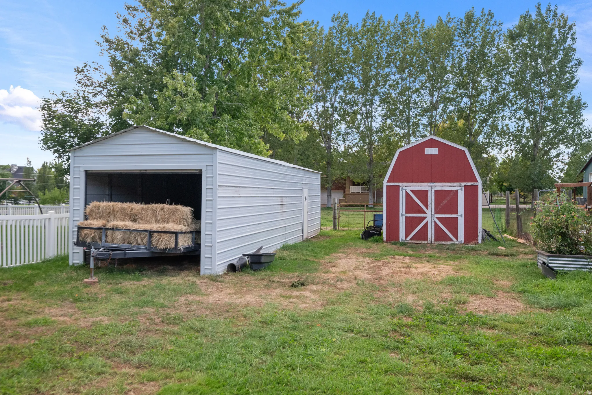 Detached metal carport, red barn-style shed, and white picket fencing define the property