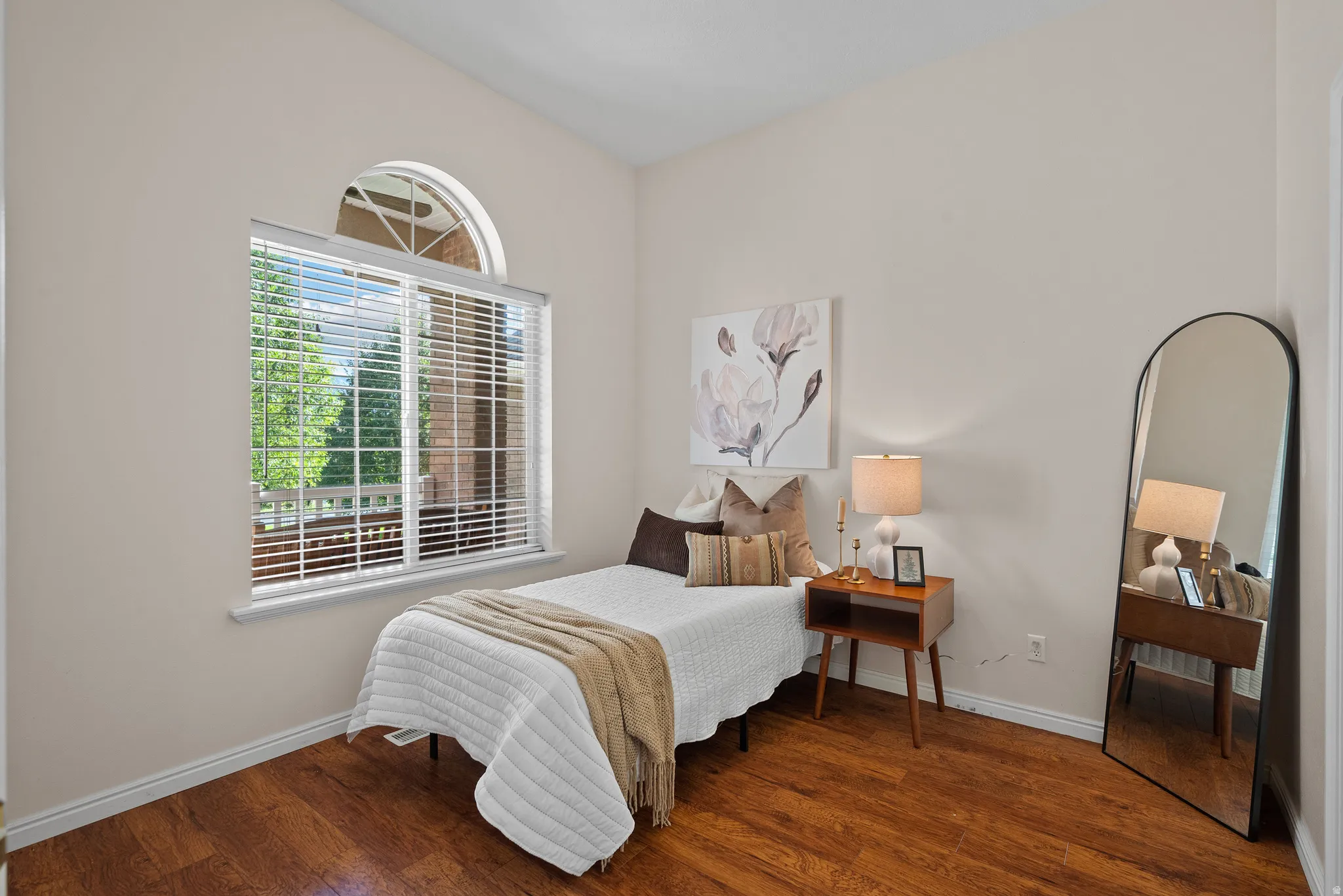 Room featuring wood-finish flooring, a large window with blinds, an arched transom window, and neutral wall paint