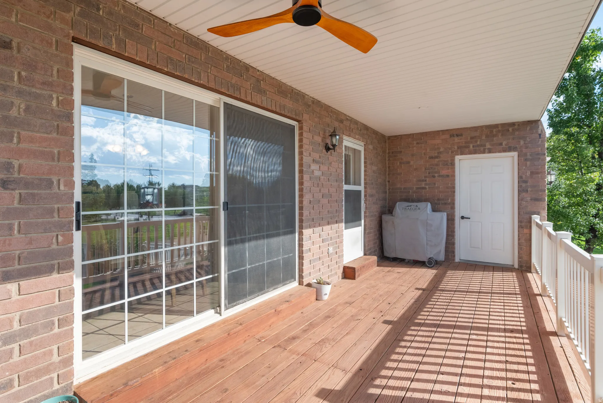 Spacious covered deck with wood-finish flooring, brick exterior, white railing, and a wood ceiling fan
