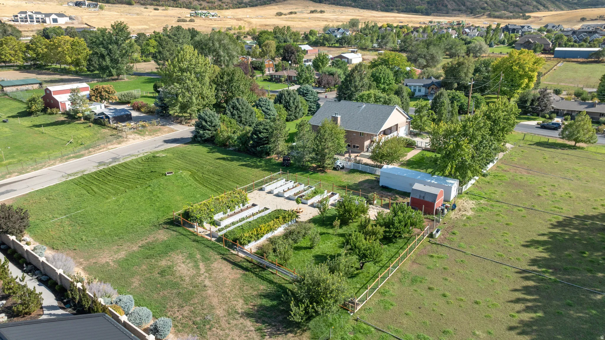 Expansive property featuring a cultivated garden, mature trees, and a brick exterior dwelling with a gray roof