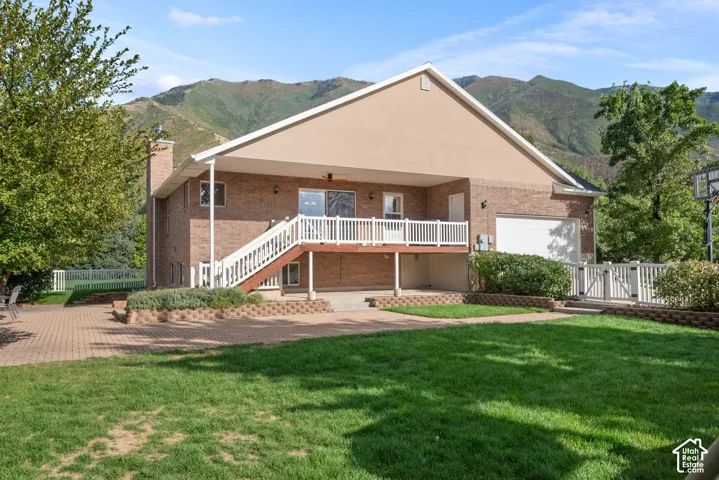 Brick exterior with covered deck, lower patio, attached two-car garage, and expansive lawn