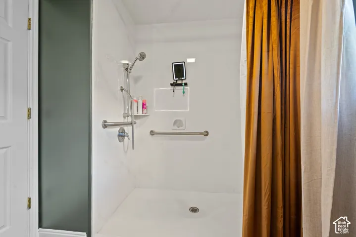 White shower stall featuring a built-in shelf, grab bars, and a handheld showerhead