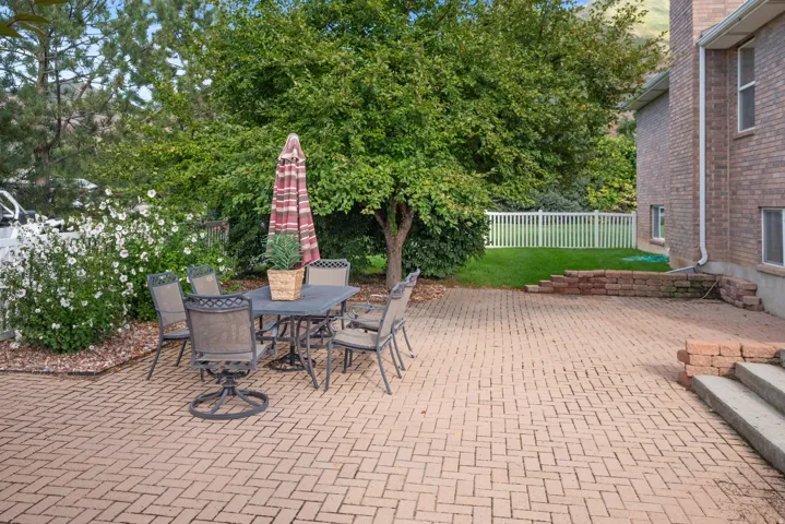 Expansive brick paver patio featuring a herringbone pattern, bordered by mature trees and lush landscaping