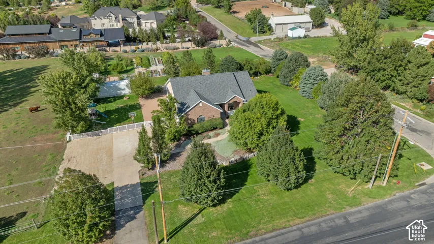 Brick exterior residence with a dark shingle roof, extensive green lawn, mature trees, and a gravel driveway