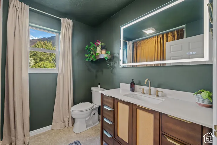 Bathroom featuring a wood-finish vanity with an integrated sink, a large back-lit mirror, and a window