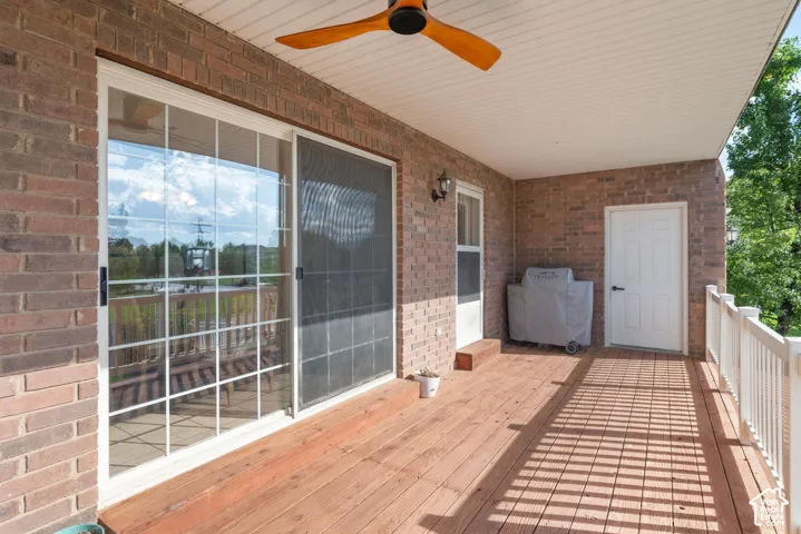 Spacious covered deck with wood-finish flooring, brick exterior, white railing, and a wood ceiling fan