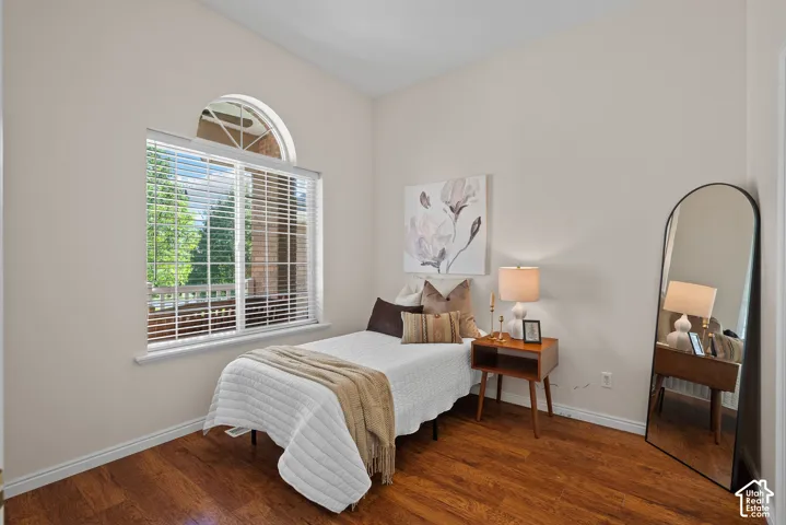 Room featuring wood-finish flooring, a large window with blinds, an arched transom window, and neutral wall paint