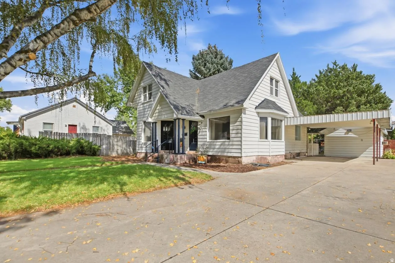 White siding exterior with a dark shingle roof, a bay window, and a covered carport