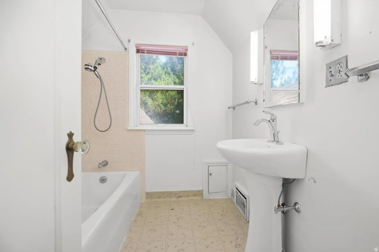 Pedestal sink with chrome faucet, built-in bathtub, and window with privacy blinds