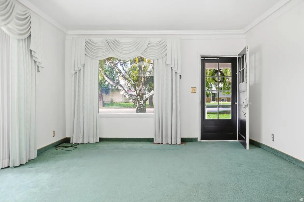 White walls with crown molding, large window with drapes, and a glass-paneled entry door