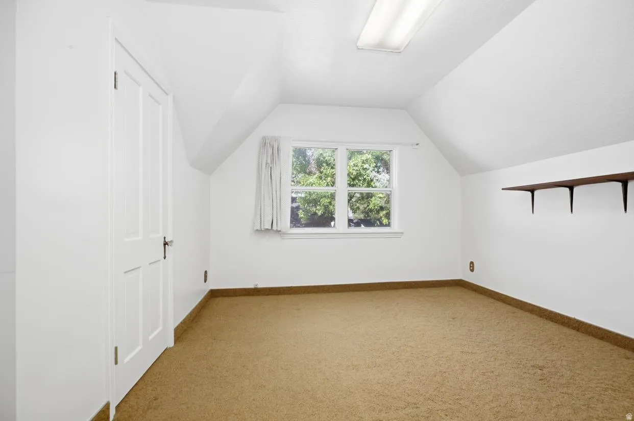 Attic room featuring a single window, built-in shelving, a flush-mount overhead light fixture, and sloped ceilings