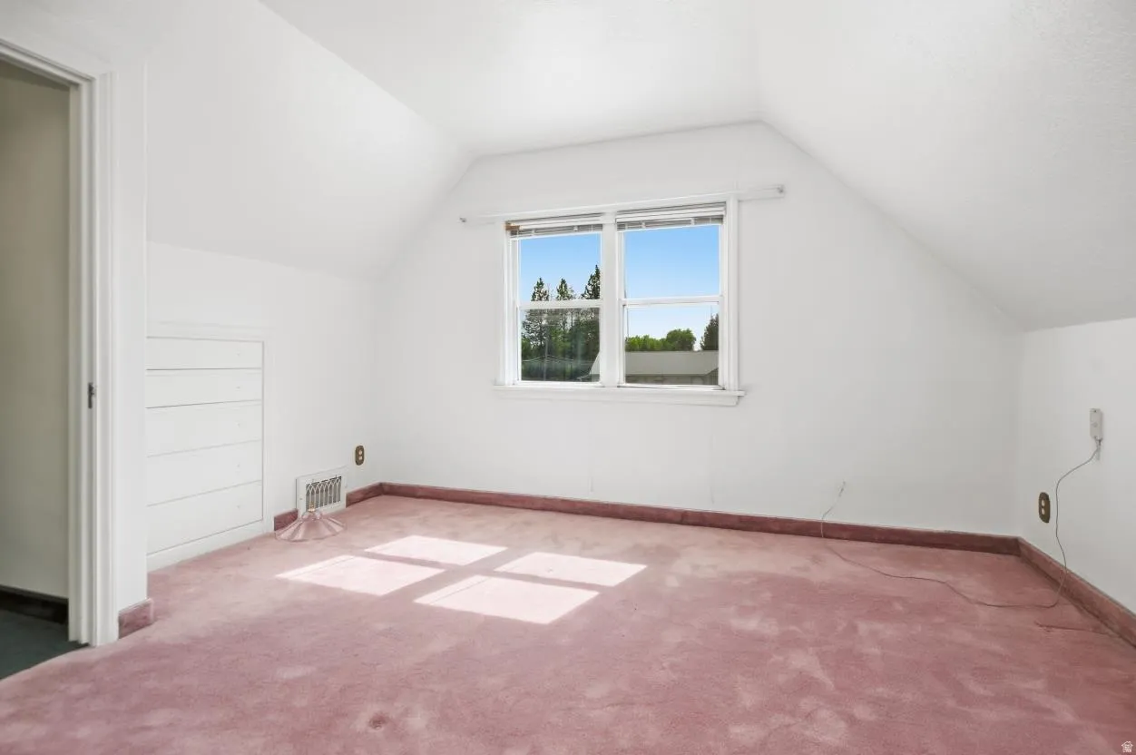 Sloped ceilings, window with outdoor scenery, wall-mounted storage, and pink carpet flooring
