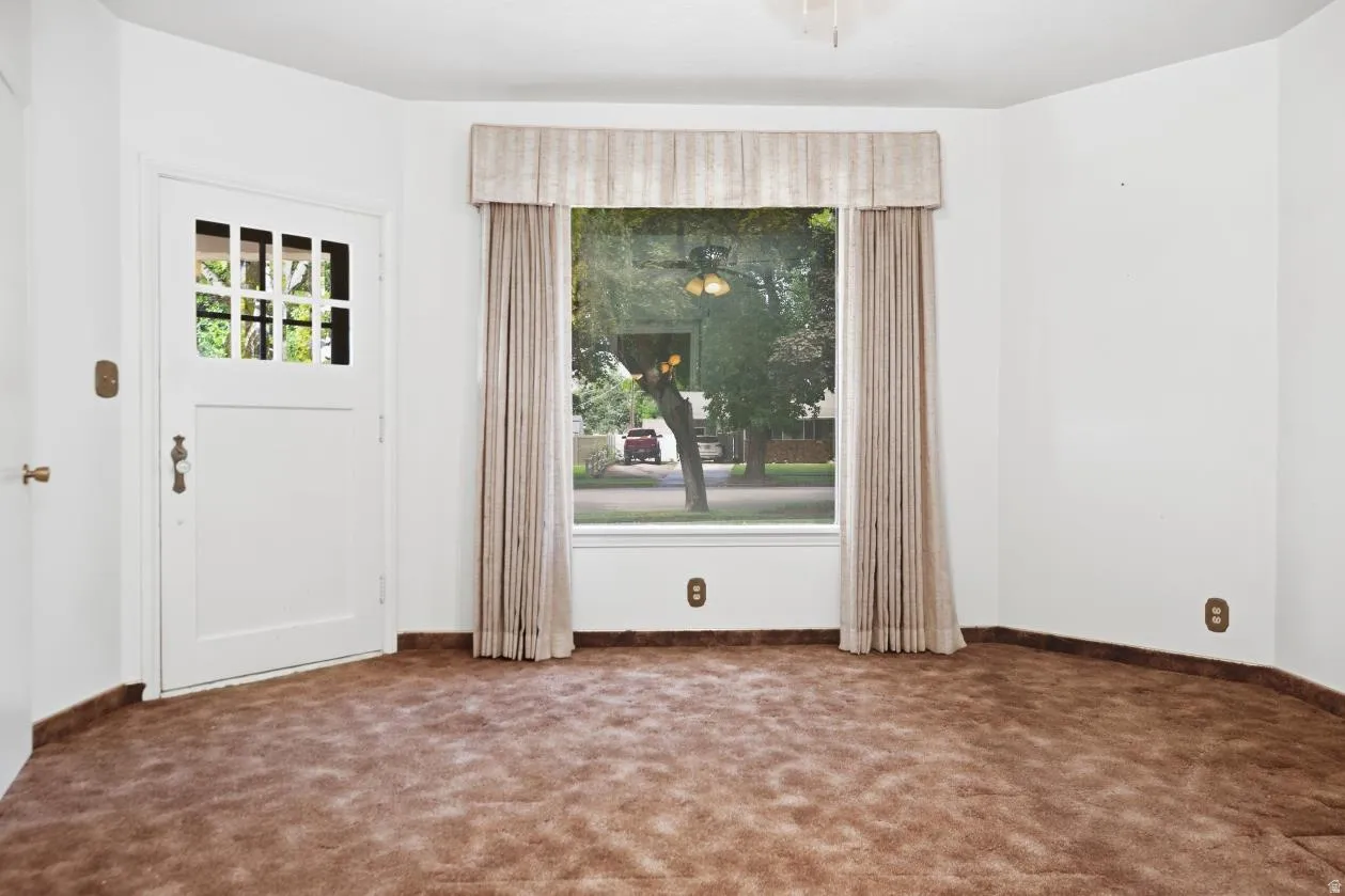White paneled door with glass inserts, bay window with neutral drapes, ceiling fan, and brown carpeting- has its own entrance by front door