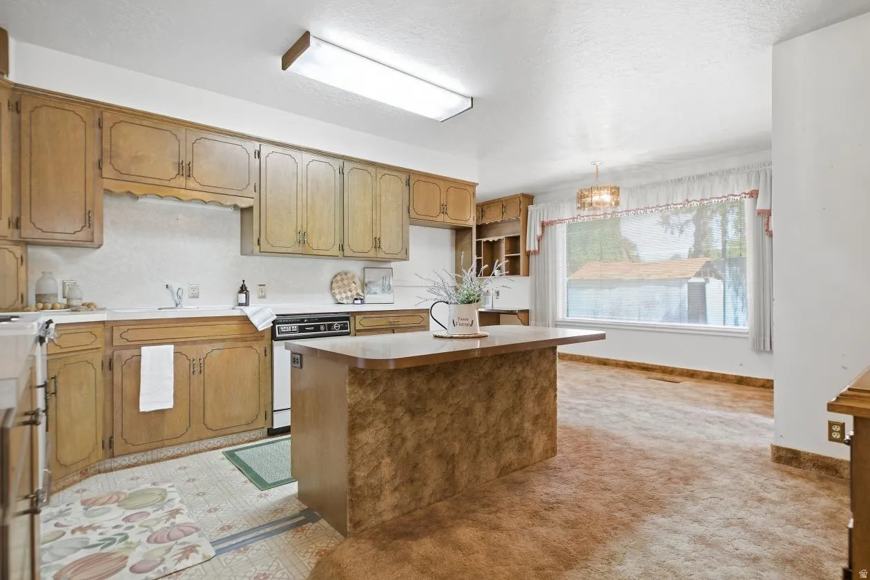 Wood-finish cabinetry, white countertops, built-in dishwasher, kitchen island with countertop, and overhead lighting fixtures