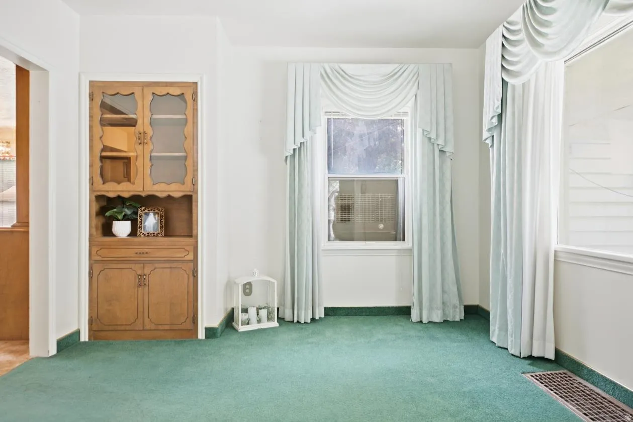 Built-in wooden cabinetry with glass-paneled doors, a single window, and wall-to-wall carpeting