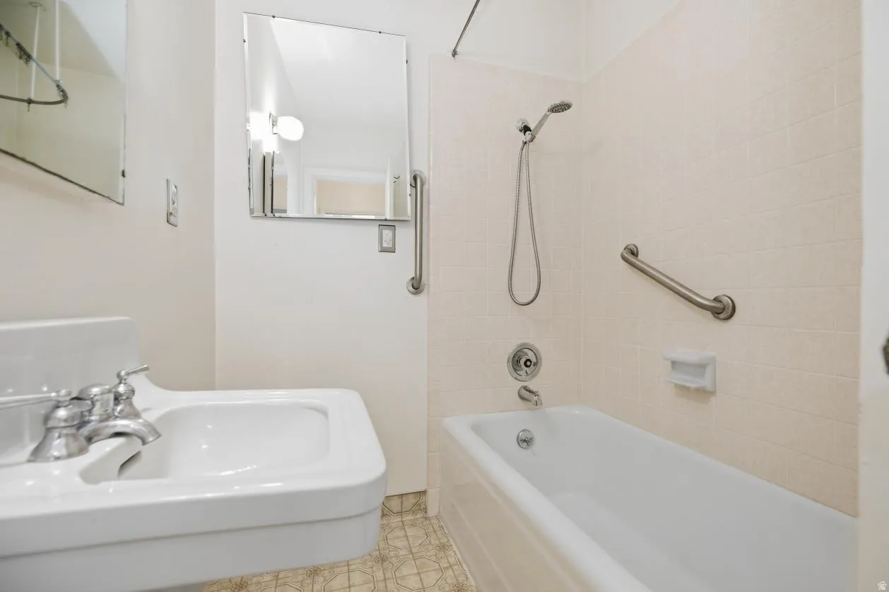White pedestal sink with chrome fixtures, full-size bathtub with handheld shower, and wall-mounted grab bar