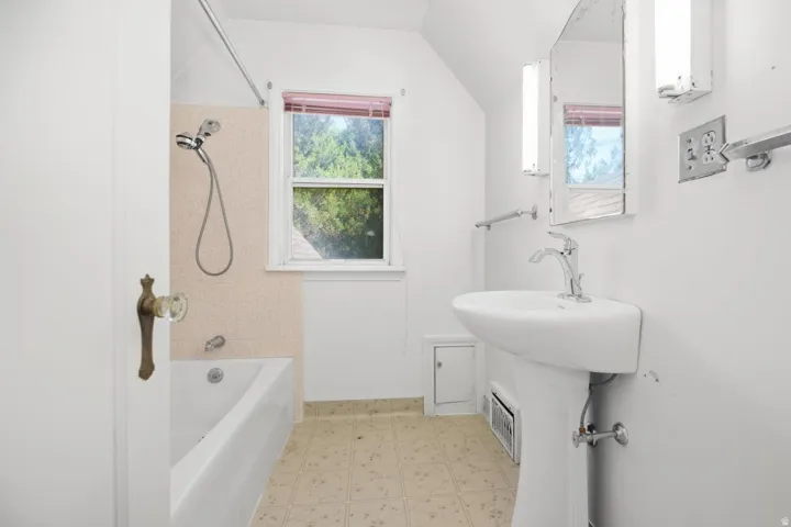 Pedestal sink with chrome faucet, built-in bathtub, and window with privacy blinds