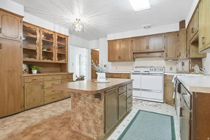 Kitchen featuring wood-finish cabinetry, a central island with a wood-finish countertop, white appliances, and built-in glass-front display cabinets