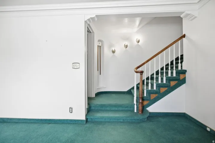 Staircase with wood-finish handrail, white balusters, and green carpeted treads