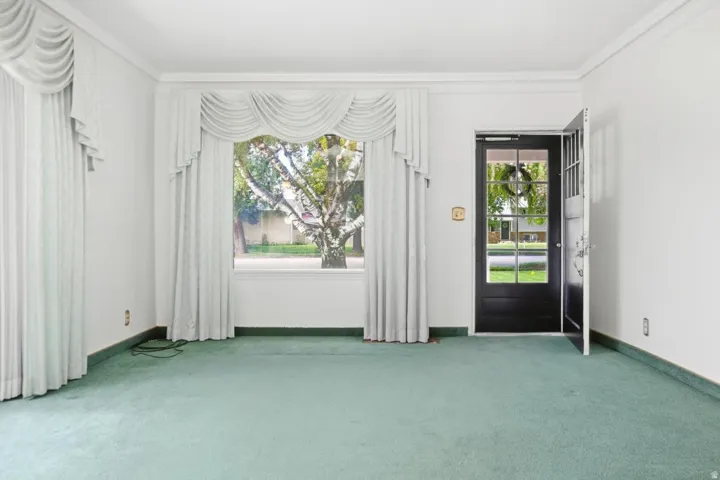 White walls with crown molding, large window with drapes, and a glass-paneled entry door