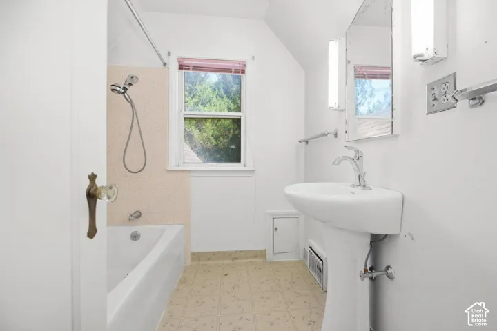 Pedestal sink with chrome faucet, built-in bathtub, and window with privacy blinds