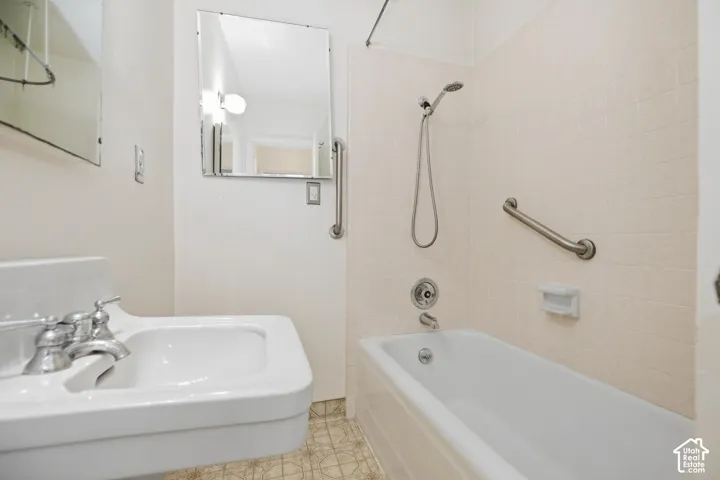 White pedestal sink with chrome fixtures, full-size bathtub with handheld shower, and wall-mounted grab bar