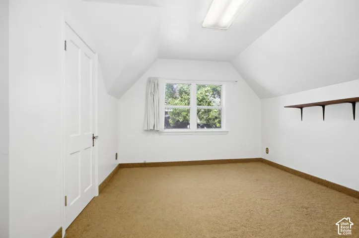Attic room featuring a single window, built-in shelving, a flush-mount overhead light fixture, and sloped ceilings