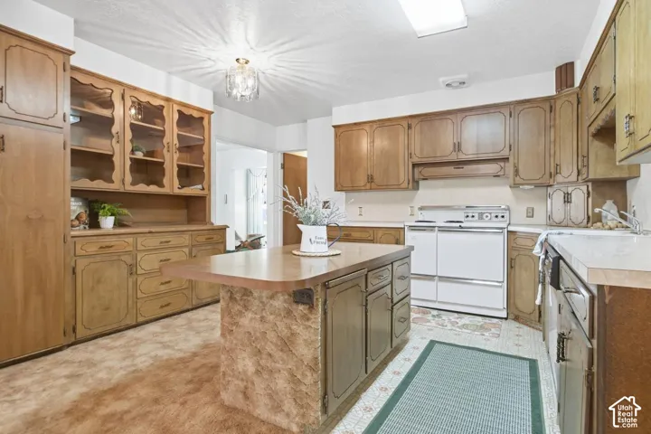 Kitchen featuring wood-finish cabinetry, a central island with a wood-finish countertop, white appliances, and built-in glass-front display cabinets