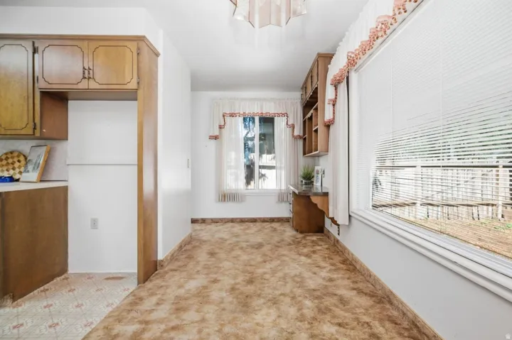 Light-filled room featuring a broad window, built-in wooden shelving, wood-finish cabinetry, and neutral wall paint
