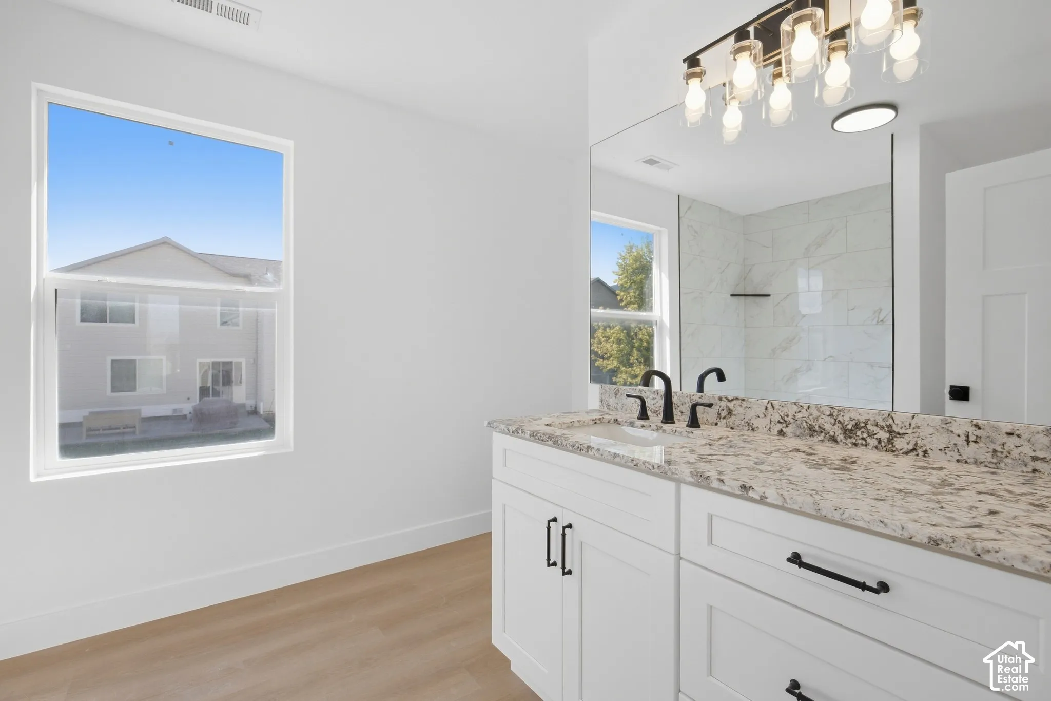 Dual vanity with stone countertop, matte black fixtures, white cabinetry, and wood-finish flooring