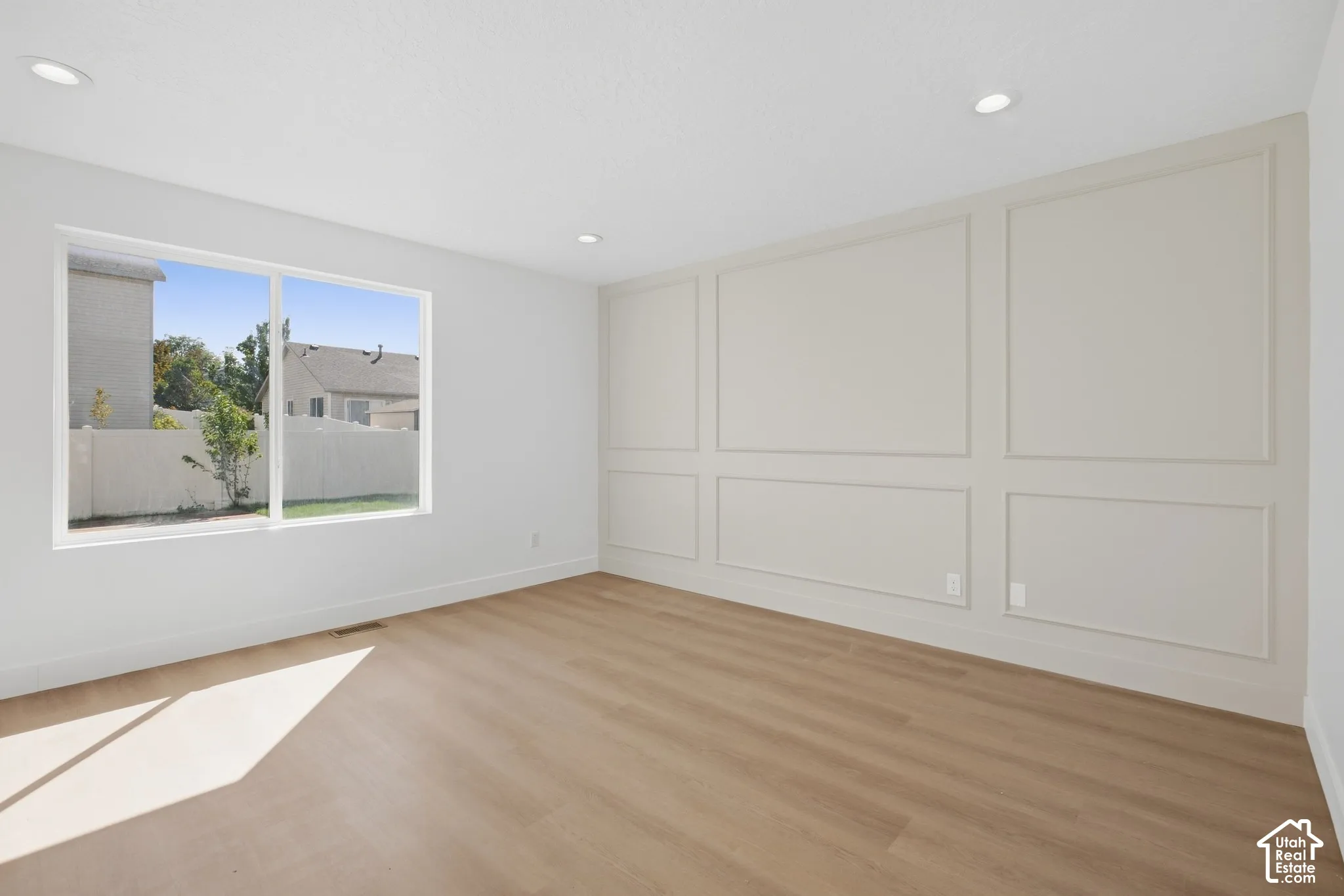 White paneled accent wall, wood-finish flooring, recessed lighting, and a large window