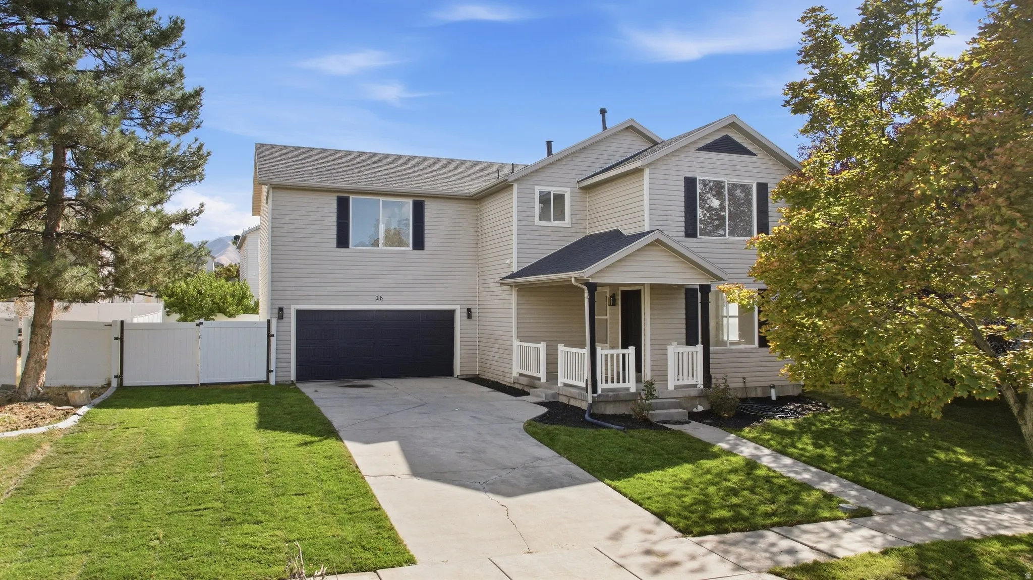Two-story residence featuring light-colored siding, a covered front porch with white railings, a dark-toned garage door, and a concrete driveway